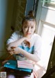 A woman sitting on a window sill holding a stack of books.