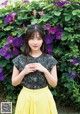 A woman standing in front of a bush of purple flowers.